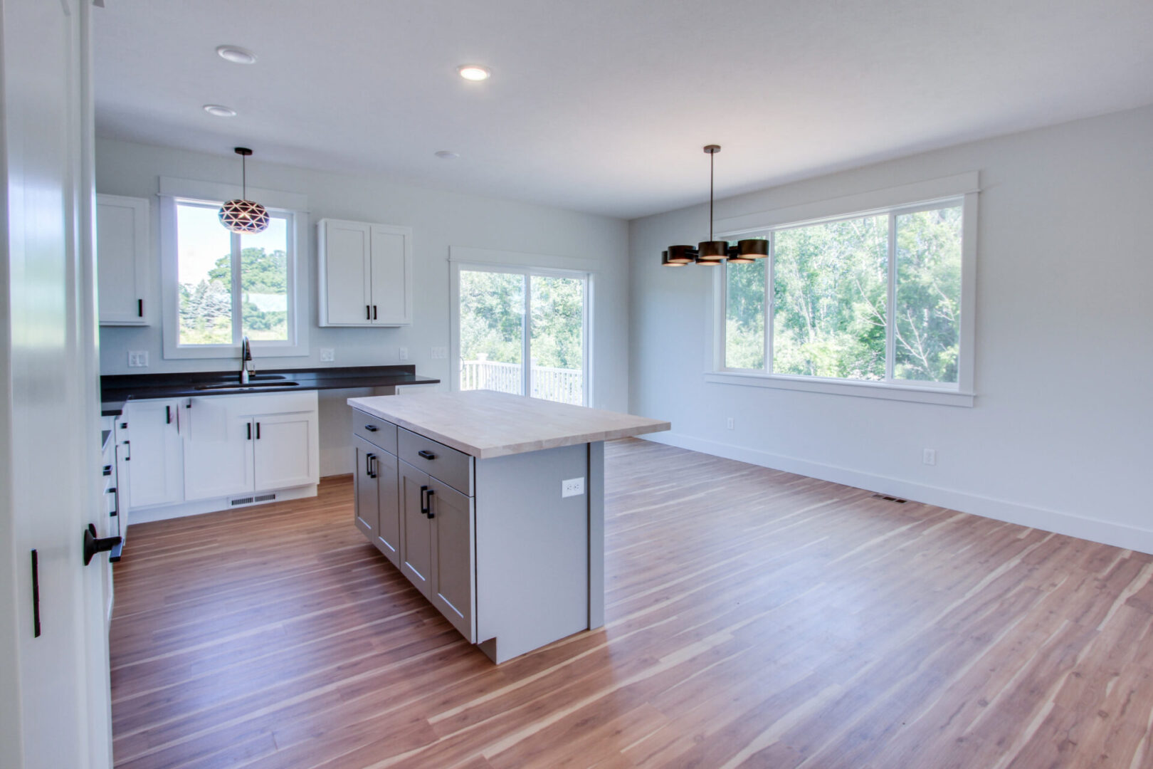 A spacious kitchen with white walls, large windows, and wooden floors